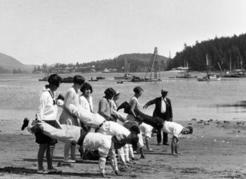 Wheelbarrow race at Clayoquot Days on Stubbs Island, early 1930s. People travelled from all over Clayoquot Sound to participate in this May 24 event, the largest, most important gathering of the year. Sporting events of all kinds, boat races, and a community picnic drew hundreds of people: aboriginals, Japanese, and European settlers alike. The growing town of Tofino can be seen in the background, also Bill Bond’s pile driver. Monks collection, courtesy of Lois Warner