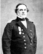 Middle-aged man with sideburns wearing a coat with epaulets and large buttons and a medal attached to the front, standing and looking slightly to the side
