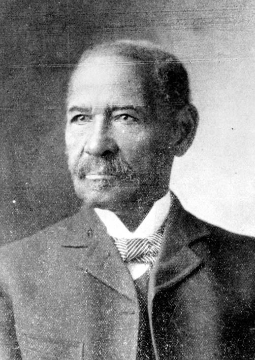 Old, dark-skinned man with closely cropped hair, a mustache and small beard wearing a blazer and a high collared shirt with a striped bow tie, looks slightly to the side