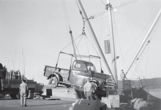A pickup truck being lifted above a dock by a boat. Three people stand around it. 