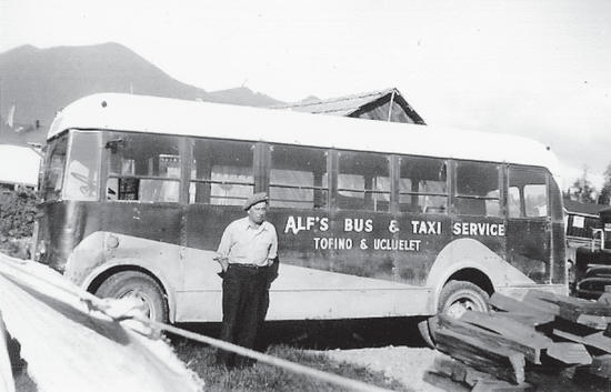 A person stands outside a bus. On the bus is the following text: Alf's Bus & Taxi Service, Tofino & Ucluelet