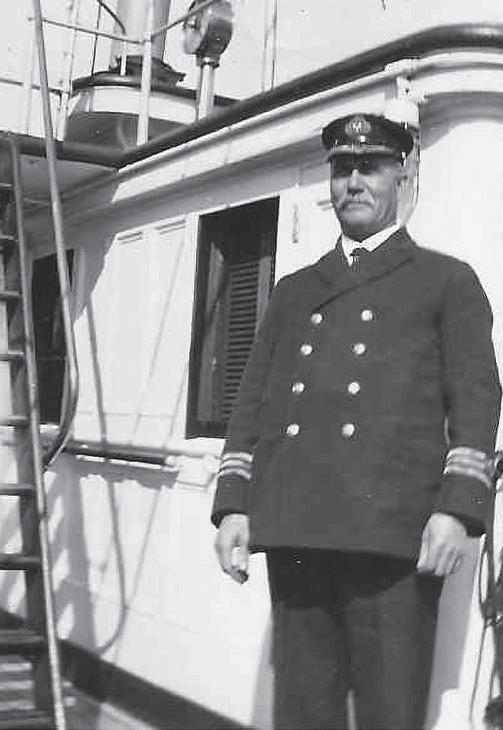 A man with a moustache and a captain's uniform standing on a boat while smiling at the camera. 