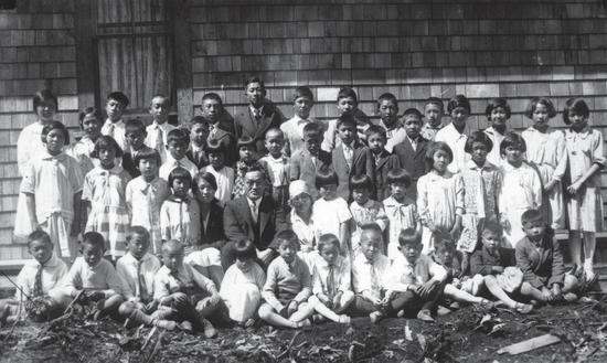 A group of about 50 people, mostly children, stand and sit posed for the camera in front of a building.