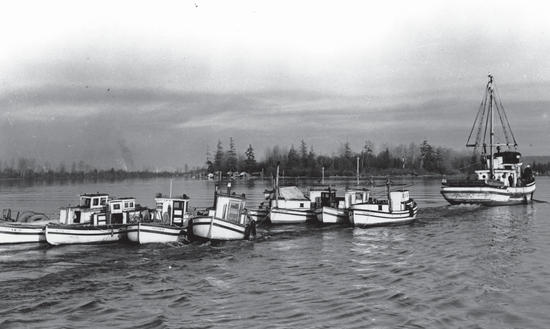 About seven boats are pulled over a body of water by a larger boat.