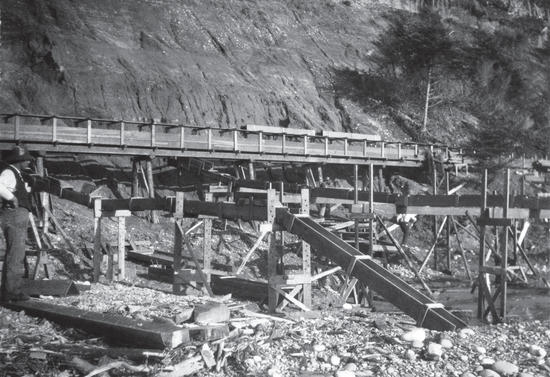 A long wooden structure built by a rock face. A man looks at the structure at the left edge of the photo. 