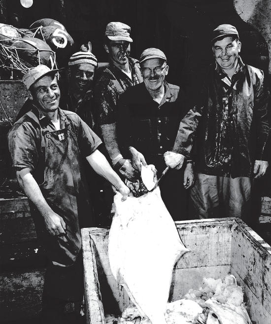 Five people smiling for the camera while holding a large halibut. 