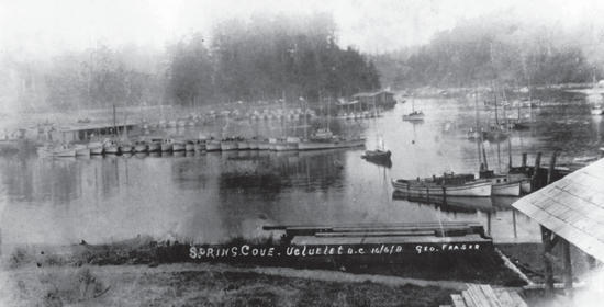 A faded photograph of a multitude of small boats parked by the shore. The text written on the photograph says the following: Spring Cove, Ucluelet B.C., 16/6/8, Geo. Fraser