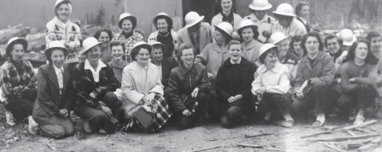 A group of more than 20 women in hats kneel while smiling at the camera.