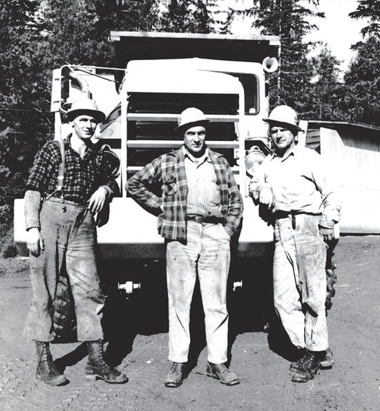 Three people in hats posed for the camera as they stand in front of a truck. 