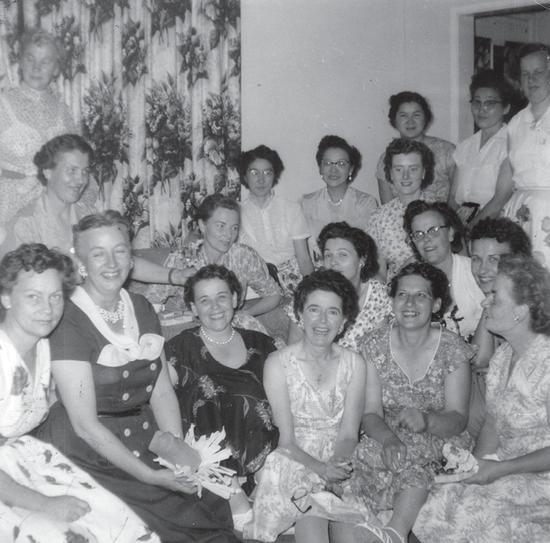 About 17 people sit and stand, posing for the camera within a room in a building.