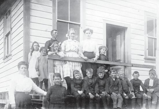About 15 people, mostly children, sit and stand while posing for the camera. They are in front of a building. 