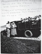 Two people stand in front of a truck. In the back of the truck is a wooden compartment holding a group of people. Text: Passengers from Maquina going on B's truck to see Long Beach. "Maquina" stayed in Ucluelet long enough for them to go see it. 