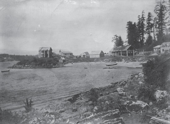An old photograph displaying the view of a collection of buildings by a body of water.