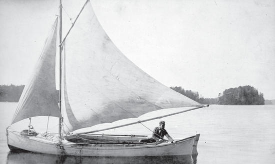 A person sitting at one end of a small sailboat on water.