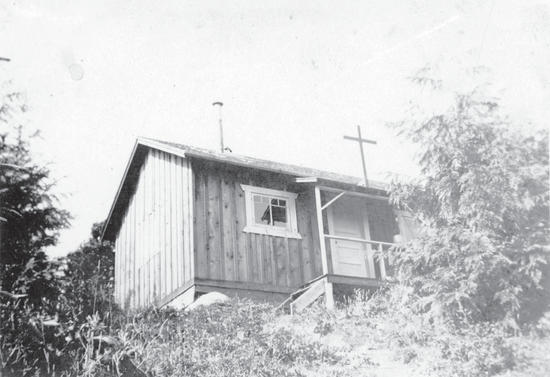 A wooden building surrounded by trees at the top of an incline as seen from below. 