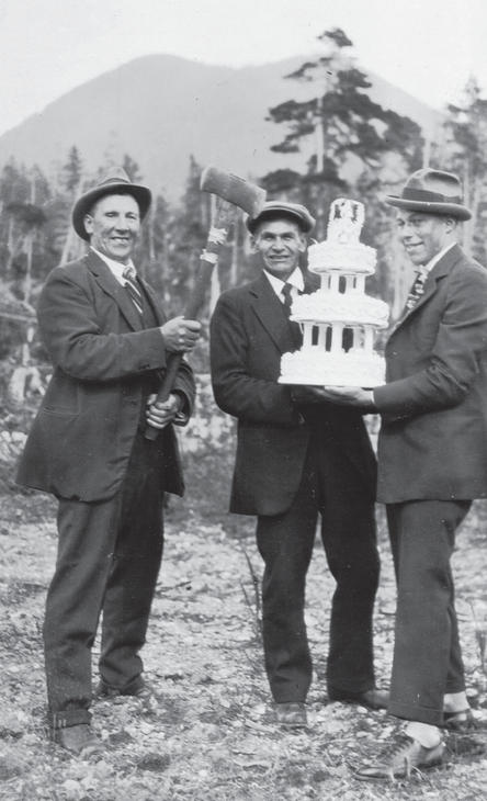 Three men in hats and three-piece suits smiling at the camera. Two of the men hold a three-tiered wedding cake while the third man holds an axe. 
