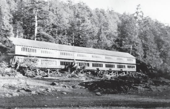 A long building by a beach. Behind the building is a forest. 