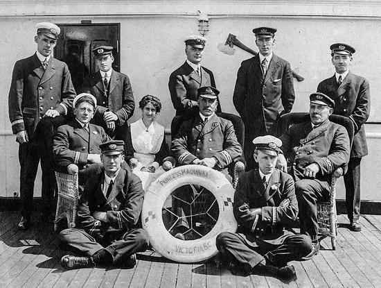 Formal group portrait photograph shows five officers standing in the back row, three officers and one nurse seated on chairs in the middle row, and two crossed-legged on the ship deck with their arms crossed. A life ring in the centre reads Princess Maquinna Victoria BC.