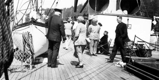 Candid photo of formally dressed passengers and the captain on deck on a sunny day.