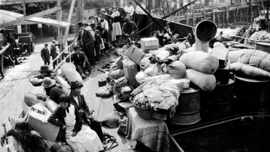 Photo of ships bow crowded with passengers and their belongings while docked.
