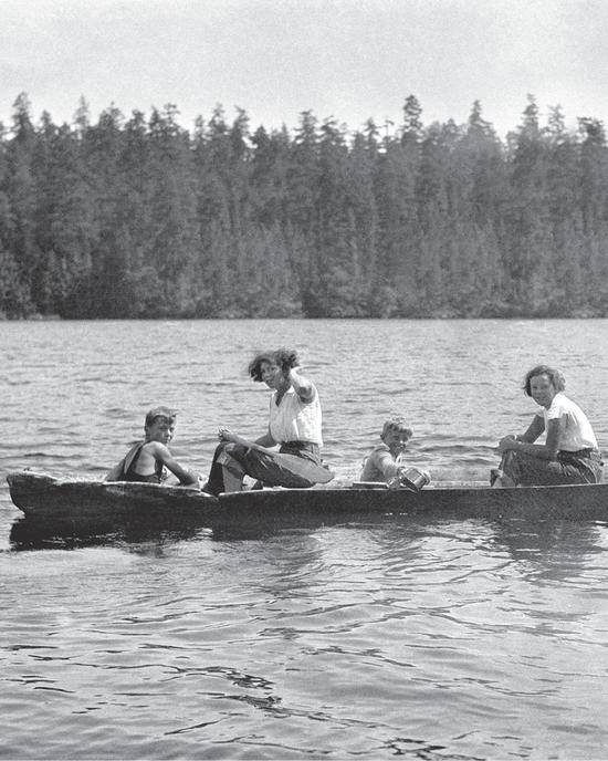Capi and three children in a canoe, with a little boy holding a bucket over the side of the boat