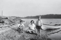 Two young boys and an older girl sit on a shell beach facing the camera