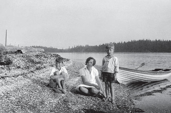 Two young boys and an older girl sit on a shell beach facing the camera