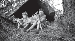 Two young boys sitting beneath a shelter made of sticks and a tarp