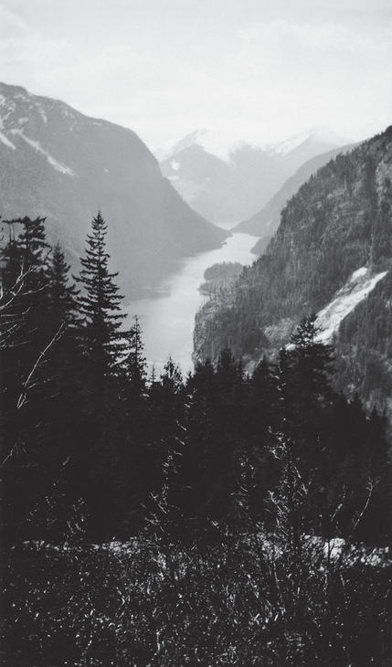 A view from high up on a mountain with trees and lake below, and mountains on either side