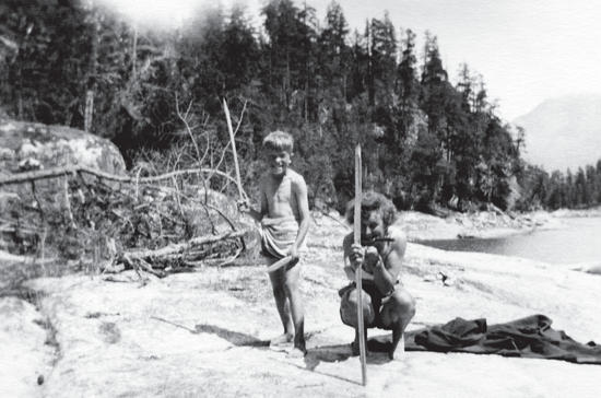 Two boys on a beach, both grinning and holding sticks