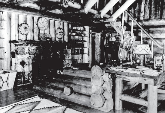The inside of a log house with a rug on the floor, lamps, and decorations on the walls