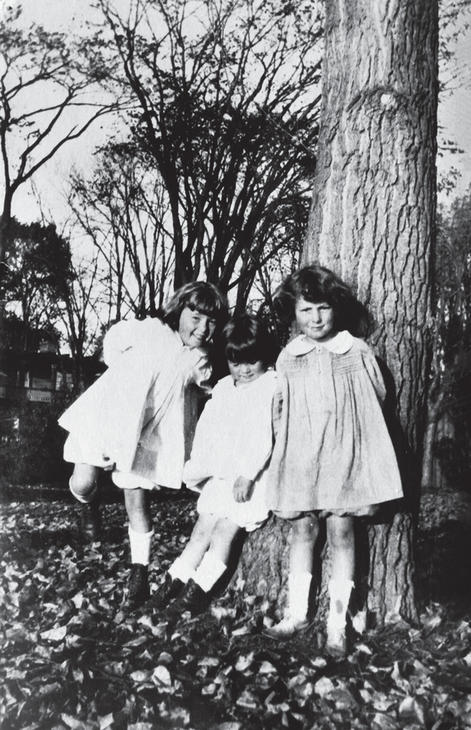 Three little girls in white dresses standing before a tree