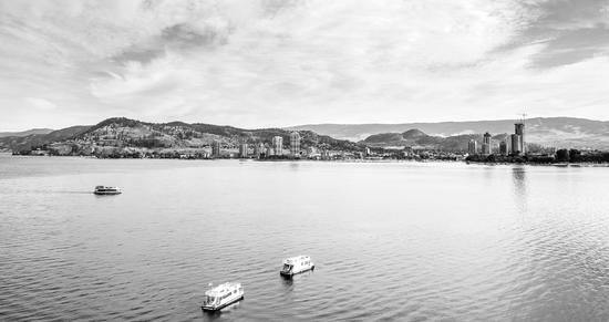 A city skyline as seen from a body of water. Three boats travel on top of the water.