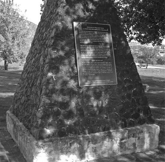 A structure made of stone in the vague shape of of pyramid. On it is a plaque with indiscernible text. In the background are trees.