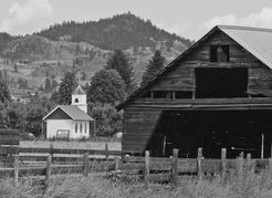 A small, white, red-roofed replica of Father Pandosy’s second church stands in a cornfield just west of the restored Mission. It marks Father Pandosy’s gravesite. As the Mission site and the fence surrounding the original graveyard deteriorated, the location of the priest’s grave became a mystery. It was not until 1983, during an archaeological dig in the area, that James Baker, a professor at Okanagan College, discovered Father Pandosy’s grave. Two other priests had been buried alongside him. The grave was on land owned by the pioneer Rampone family. Two years later, the family built a replica of Father Pandosy’s sawn wood church and transferred the gravesite and half an acre of land to the Bishop of Nelson. It is visible from the surrounding roads. | Stuart Kernaghan, xyphotos.ca