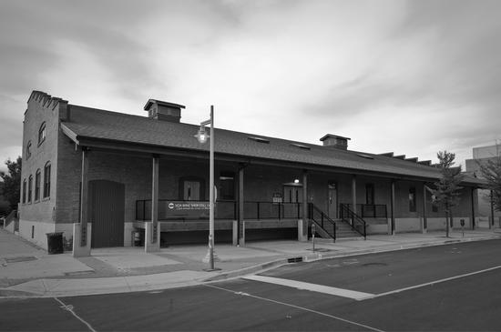 A long building made of brick as seen from the street in front of it. A staircase leads to its entrance.