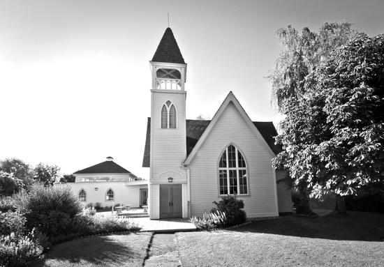 A large, light-coloured building with a spire and gothic windows surrounded by shrubbery and trees.