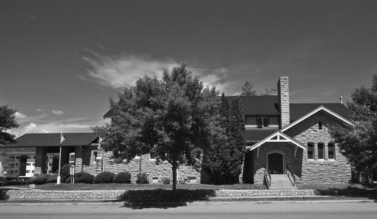 The view of a long stone church from a street. The building is obscured by a tree.