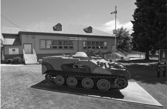Dirt paths leading to a wooden school surrounded by trees. In front, a woman and two children look at the camera.