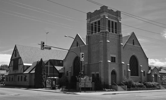 A large church with large gothic windows sits on a modern street corner. 