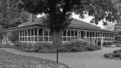 A long, one-story building with windows spanning its sides. Around it are stone pathways, trees and shrubbery.