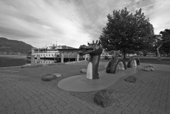 A statue of a sea serpent weaving in and out of the ground as if it were water. It is built near a dock where a boat is docked.