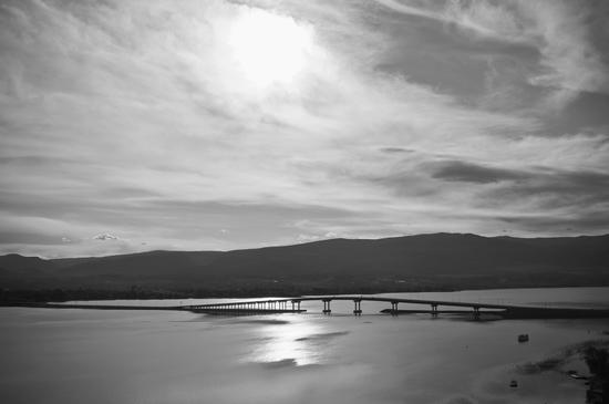 A bridge built over a body of water. In the background, a city can be faintly seen with tall hills serving as a backdrop.
