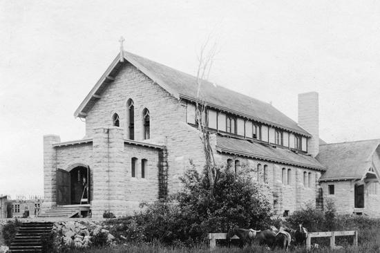 A large stone church with a large staircase leading up to its opened entrance. It is surrounded by shrubbery.