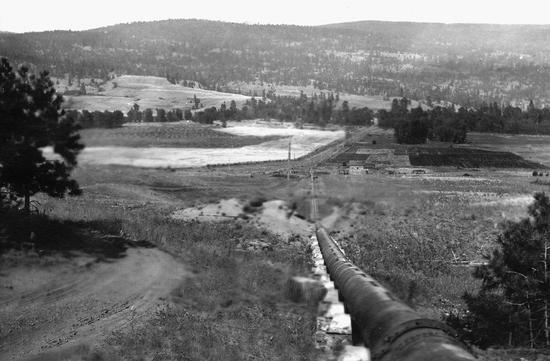 A long tube that leads to fields. In the background are hills covered in trees.