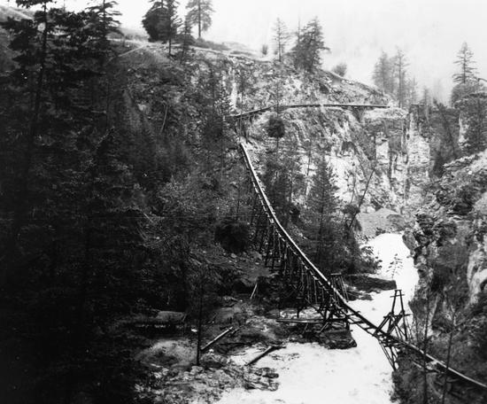 A long pipe supported by wooden beams leading down a cliffside. 