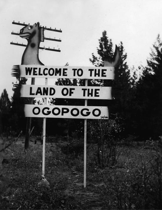 A wooden sign with the head of a sea serpent sticking out from the top. Text: Welcome to the Land of the Ogopogo