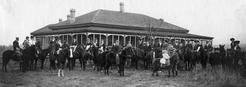A group of people sitting on horses in front of a one-story building covered in windows.