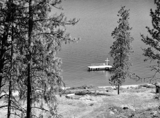 A platform raised above a body of water with a single cross on it. The platform is inaccessible as the rest of the pathway to it has been damaged. 