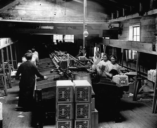 People holding boxes while packing apples within a wooden building. 